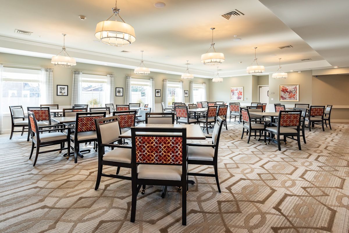An elegant dining room featuring neatly arranged tables and chairs, with modern lighting and a patterned carpet.