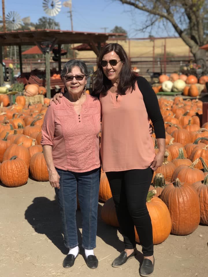 Two people standing in a pumpkin patch during autumn.
