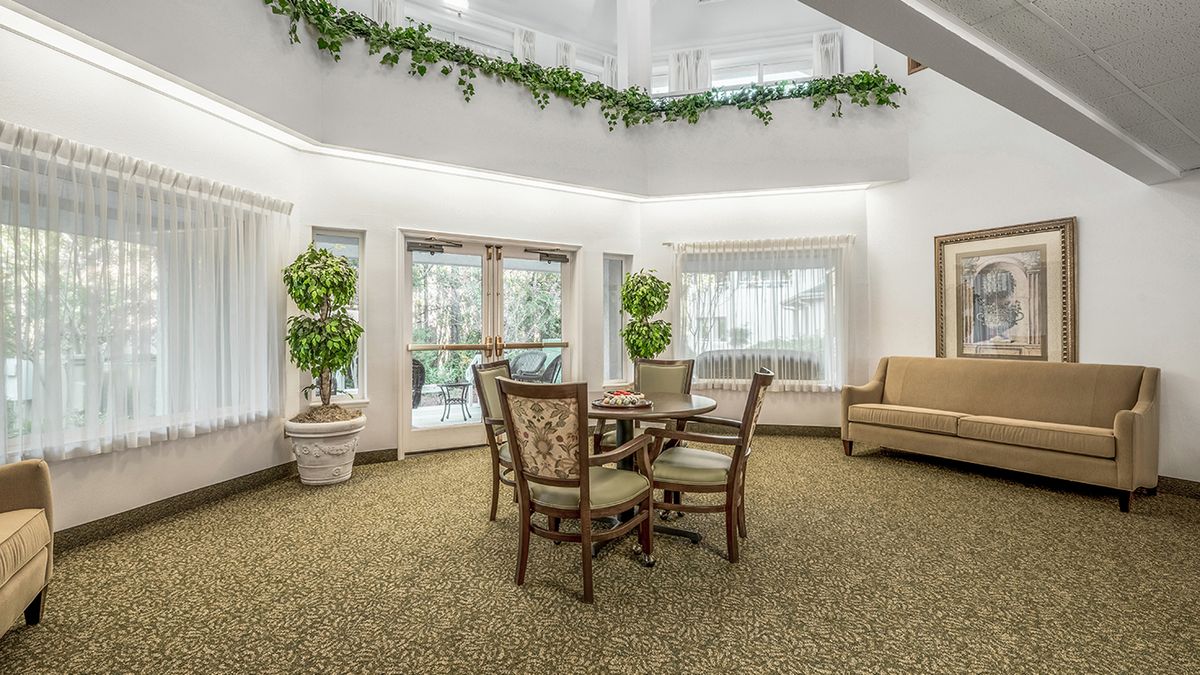 A spacious and well-lit living area featuring a table with chairs, large windows, and decorative plants.