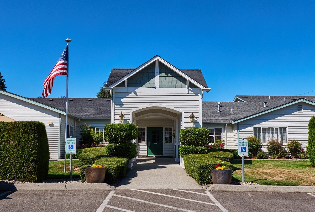 A well-maintained building entrance with an American flag and surrounding greenery on a clear, sunny day.