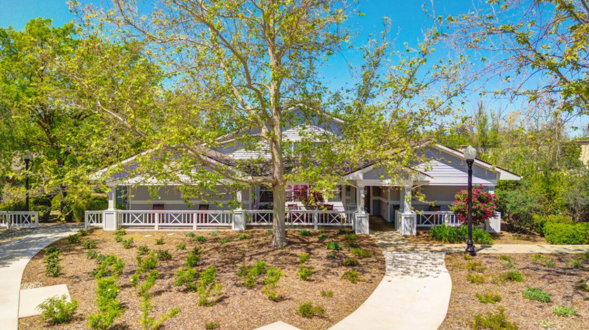 A charming house with a well-kept yard, featuring a large tree and a winding path leading to the entrance.