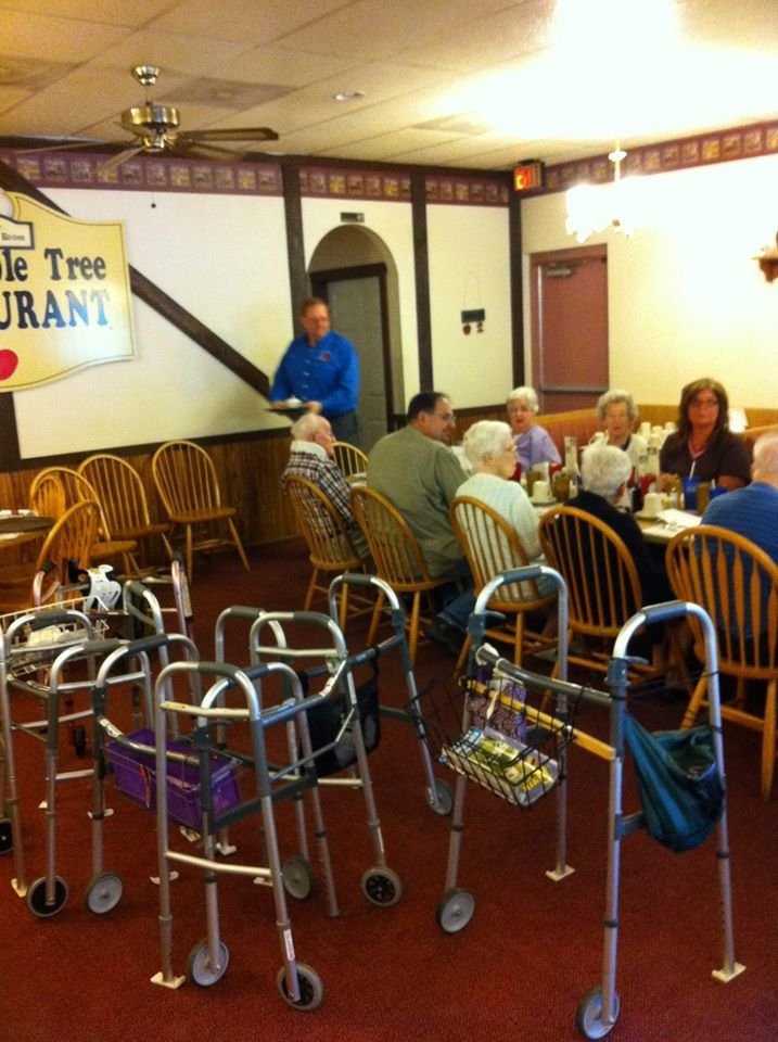 A group of seniors dining together in a restaurant with multiple walkers nearby.