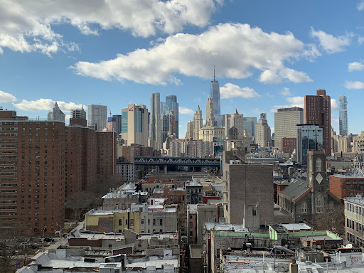 A stunning view of the New York City skyline under a bright blue sky with fluffy clouds.