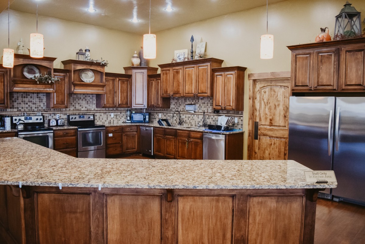 A modern kitchen with wood cabinets and a granite countertop, featuring stainless steel appliances and pendant lighting.