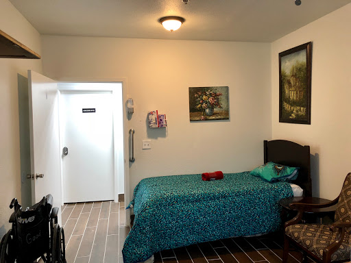 A cozy room featuring a bed with green bedding, artwork on the wall, and a wheelchair, providing a comfortable living space.