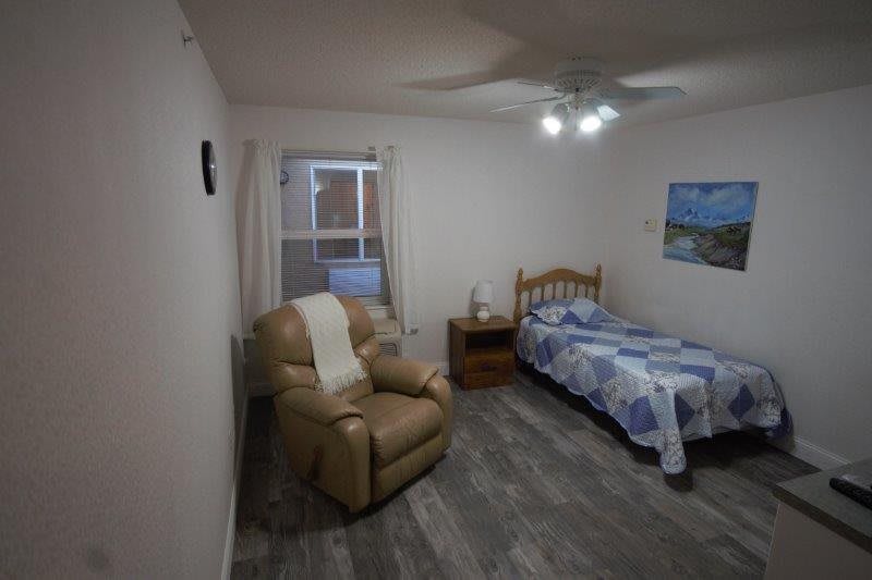 A cozy bedroom with a single bed, reclining chair, and a nightstand.