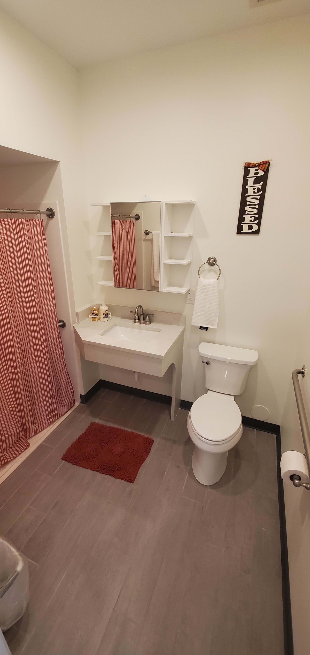 A tidy bathroom with a red shower curtain, white sink, toilet, and mirror.