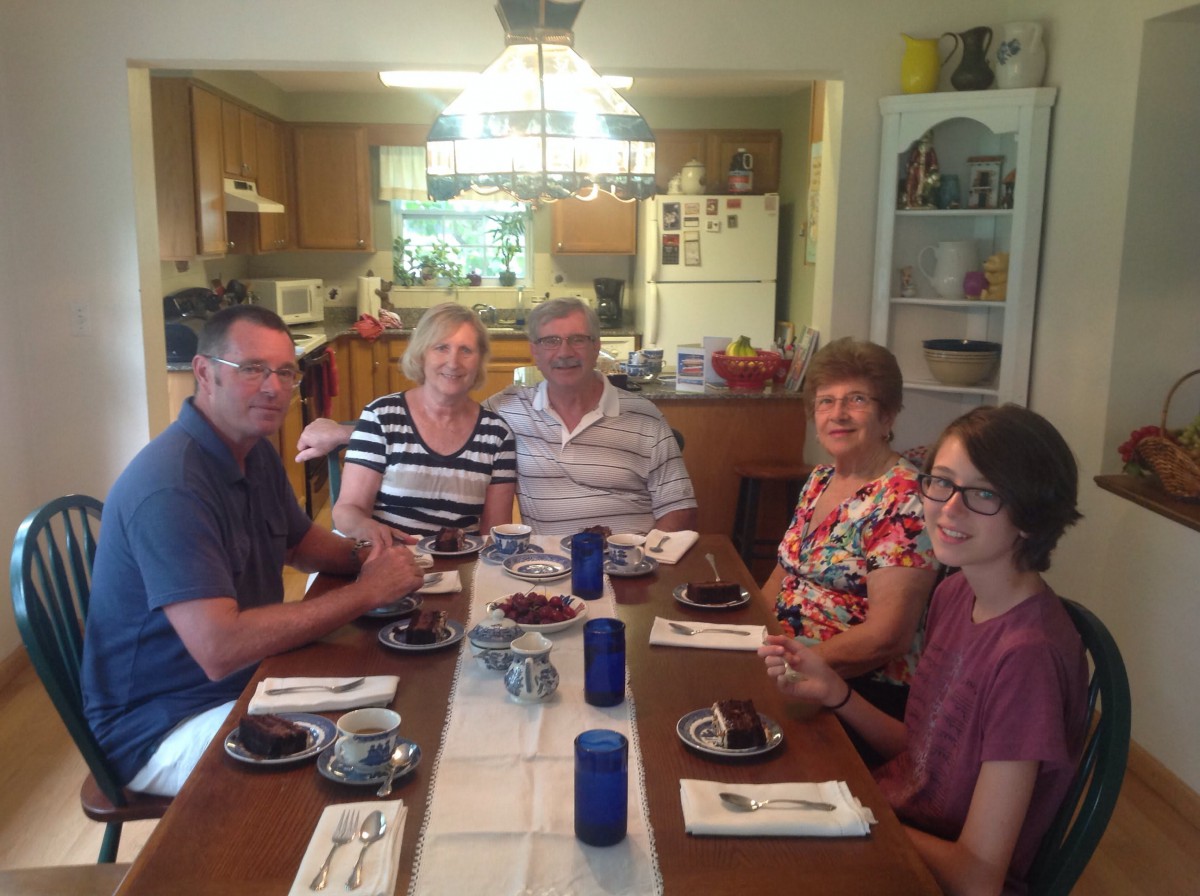 A group of people sitting around a dining table ready for a meal in a kitchen setting.