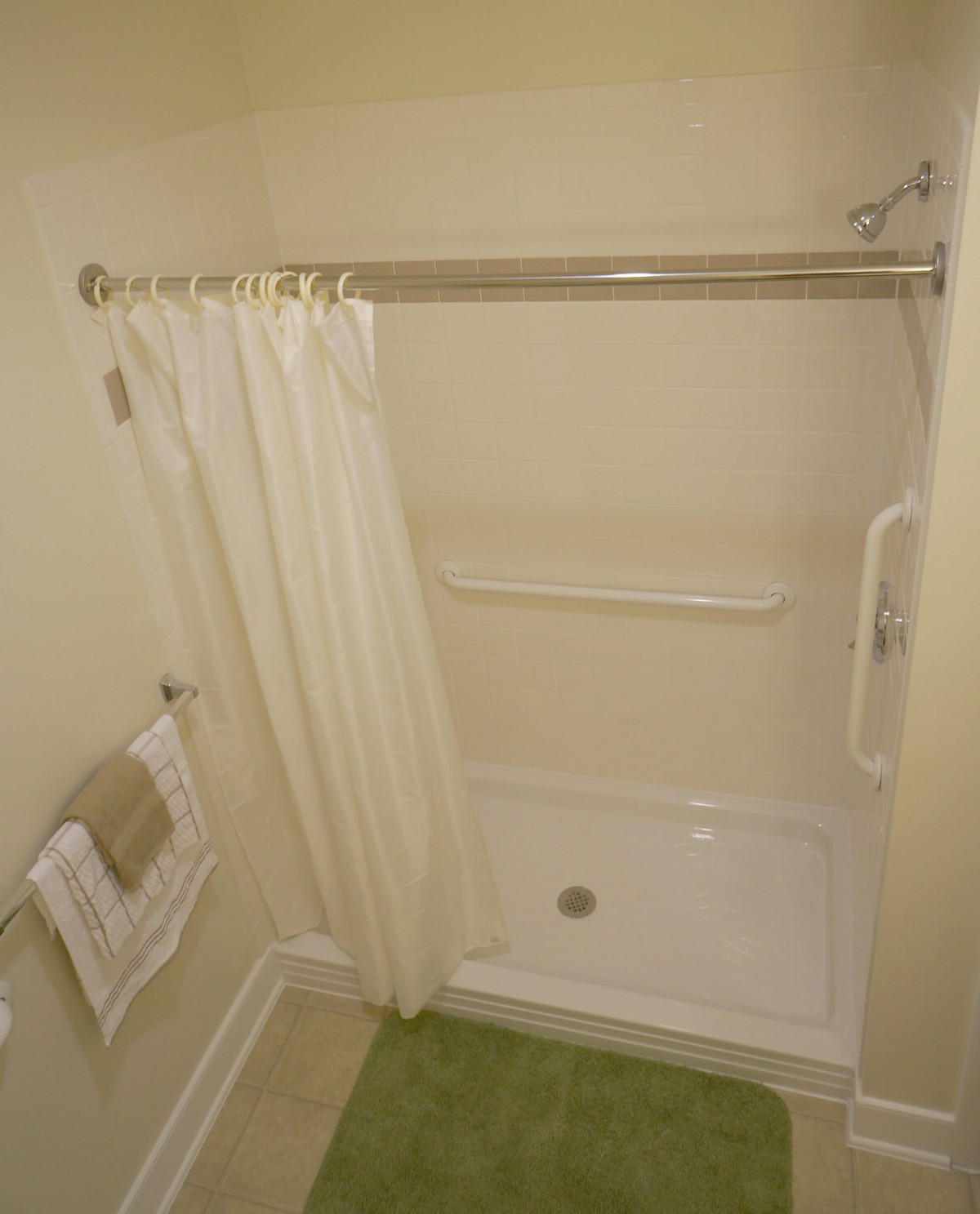A bathroom with a shower and white curtain, featuring a grab bar for safety.