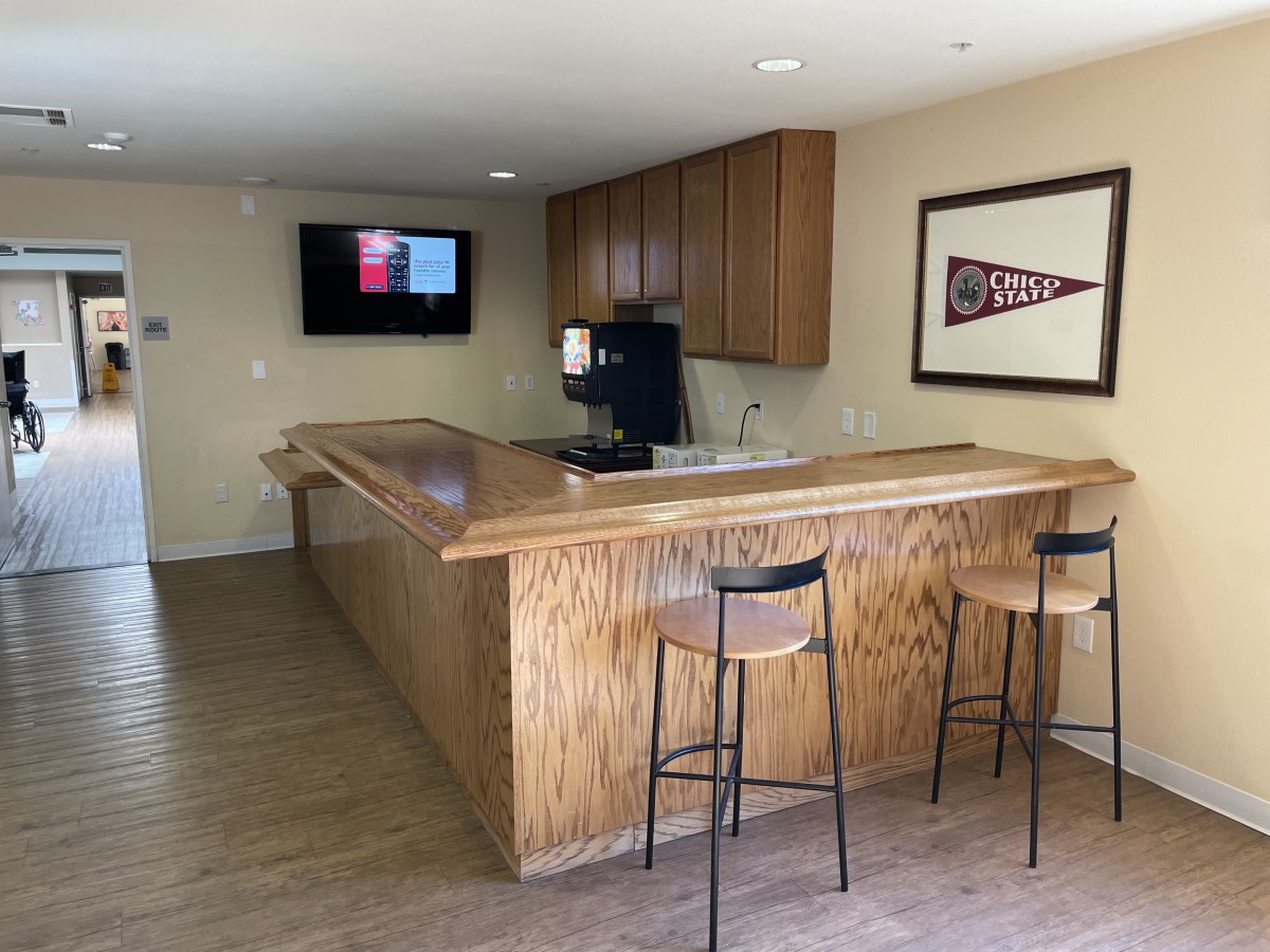 A cozy home bar setup with wooden counters and stools, featuring a mounted television and wall decor.