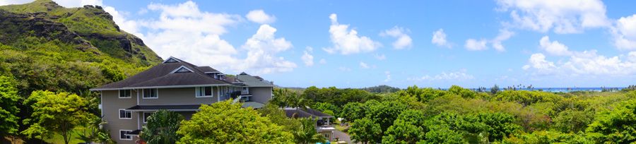 A scenic view of lush greenery and buildings under a bright blue sky with fluffy clouds.