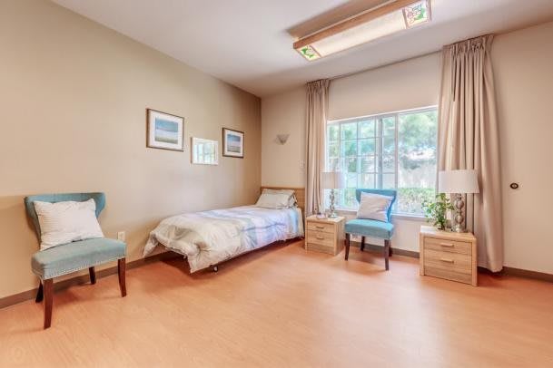 A cozy bedroom with a single bed, armchair, and large window.