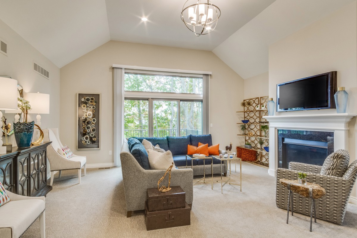 A cozy living room with a large sofa, fireplace, and a view of the trees outside.
