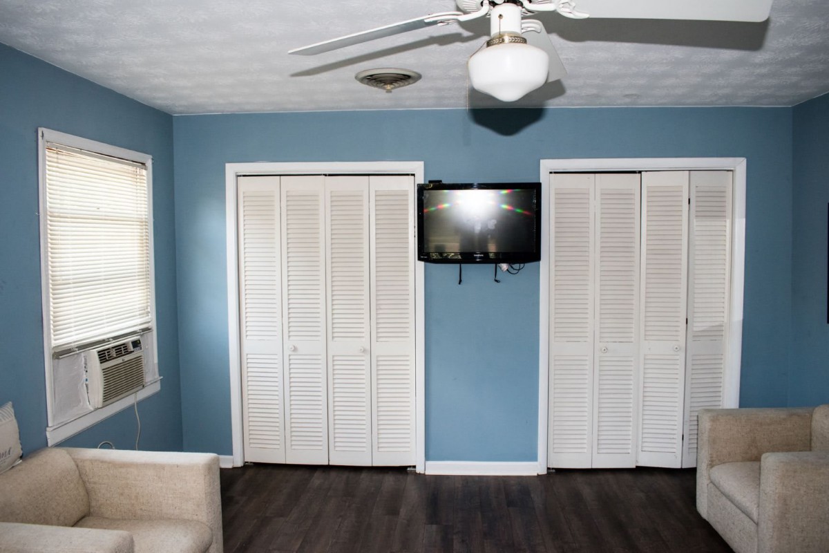 A bedroom with blue walls, featuring a ceiling fan, two closet doors, and a mounted television.