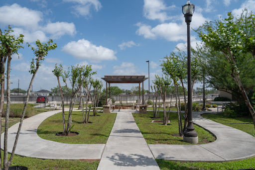 A serene park featuring well-maintained pathways, lush greenery, and a pavilion under a bright blue sky.