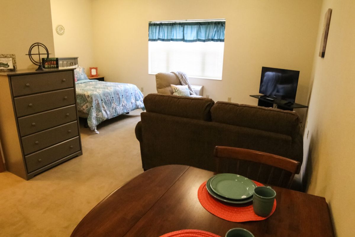 A cozy studio apartment featuring a bed, living area with a TV, and a small dining setup.