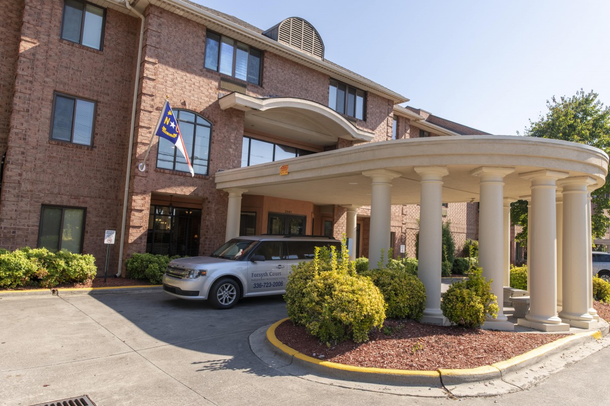 A hotel entrance with a car parked outside, featuring columns and a flag.