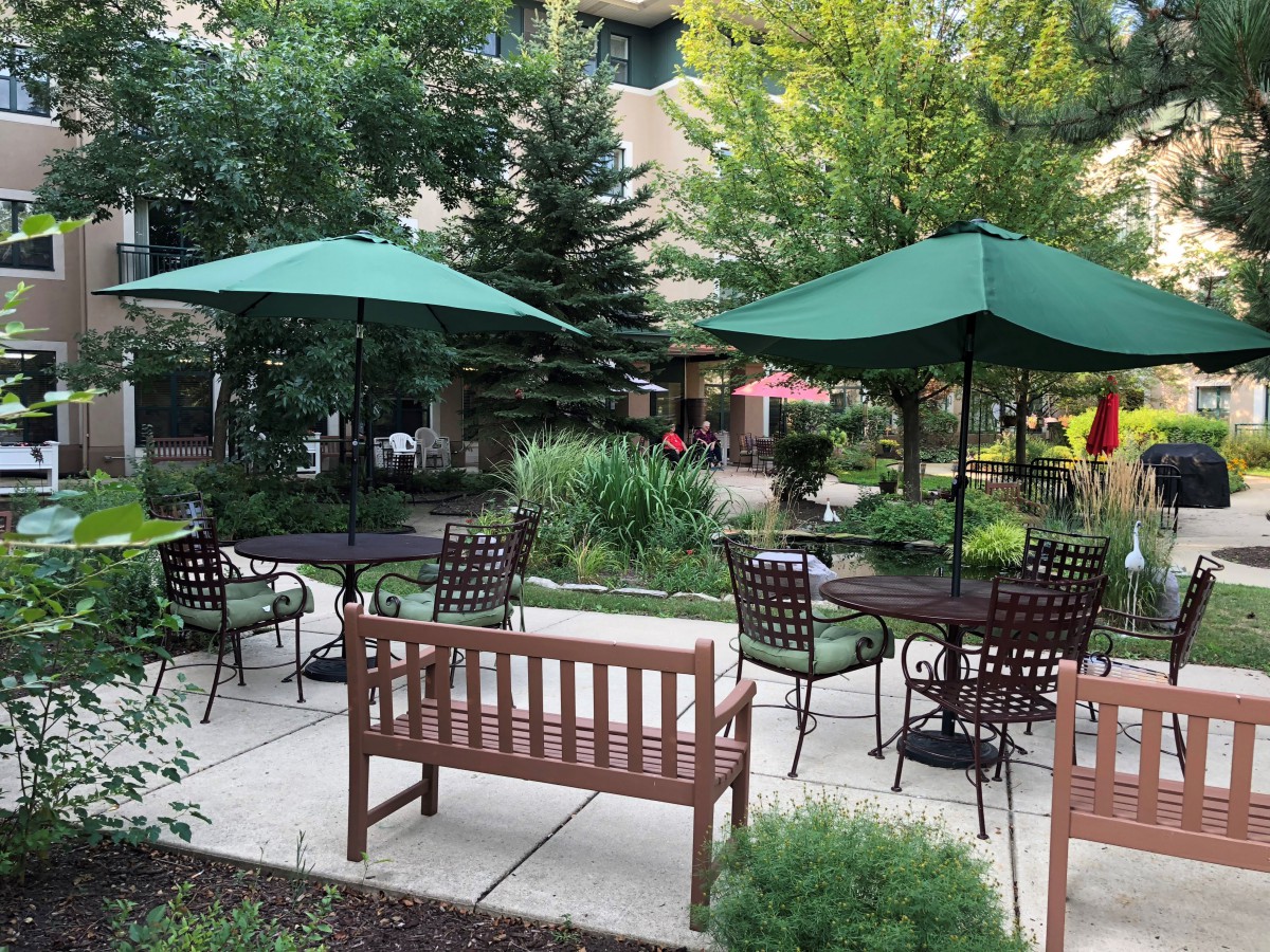 A peaceful garden patio with tables, chairs, and umbrellas surrounded by lush greenery.