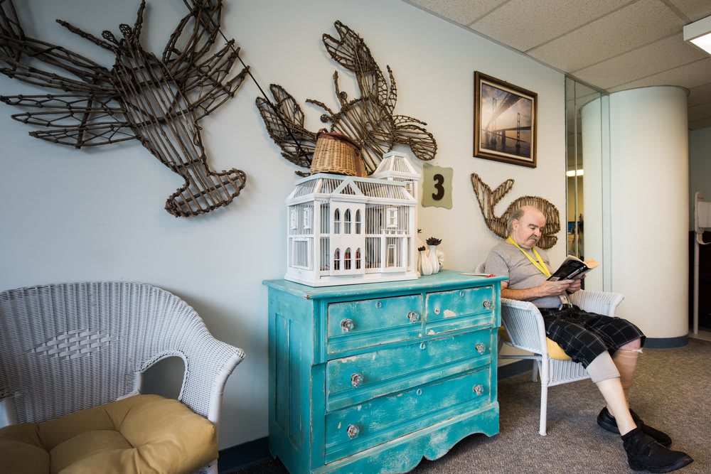 A coastal-themed waiting room featuring teal furniture and lobster decor, with a child engrossed in a book.