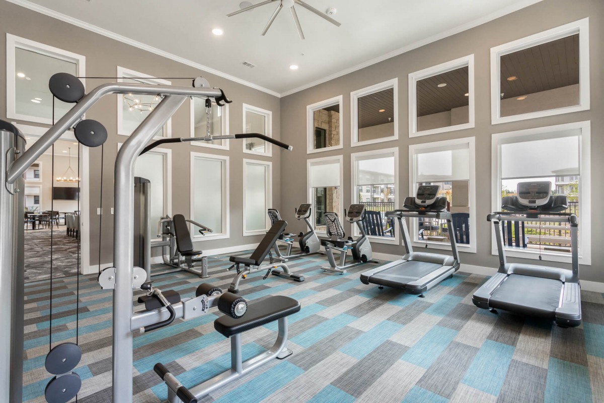 A modern gym with various exercise equipment and large windows allowing natural light.