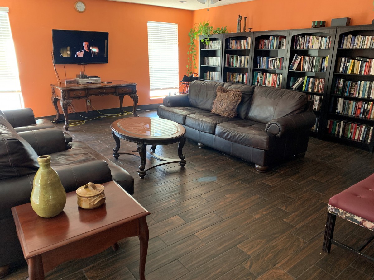 A cozy living room with orange walls, featuring a sofa, coffee table, and bookshelves filled with books.