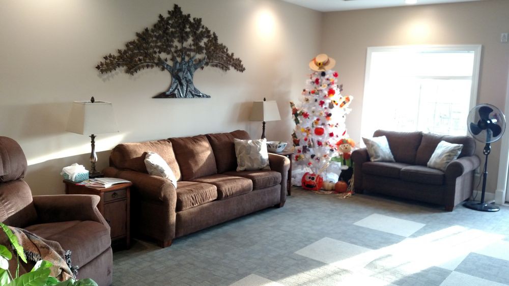 A cozy living room featuring a brown couch, a decorated Christmas tree, wall art, and ample natural light.