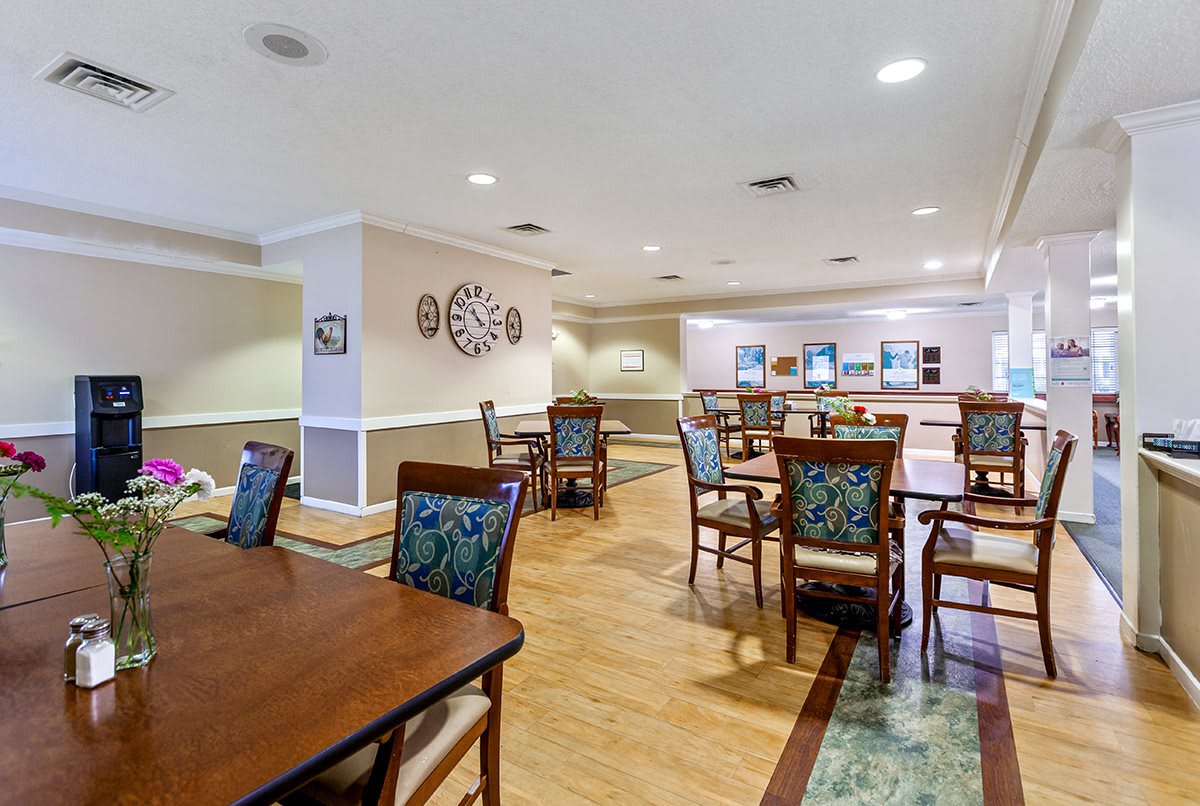 A spacious dining area with multiple tables and chairs, featuring a decorative wall clock and wooden flooring.