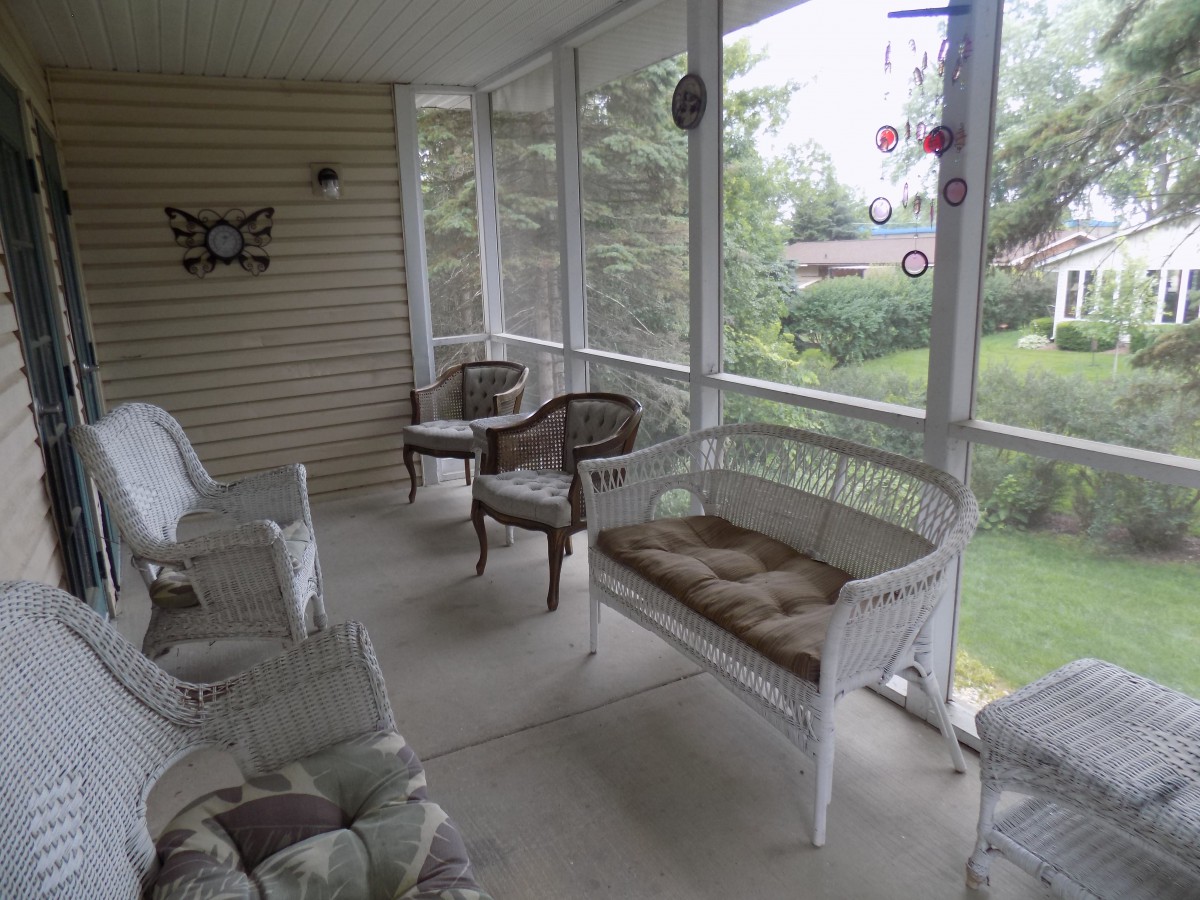 A cozy, screened-in porch with wicker furniture and cushioned seating, offering a relaxing outdoor space.