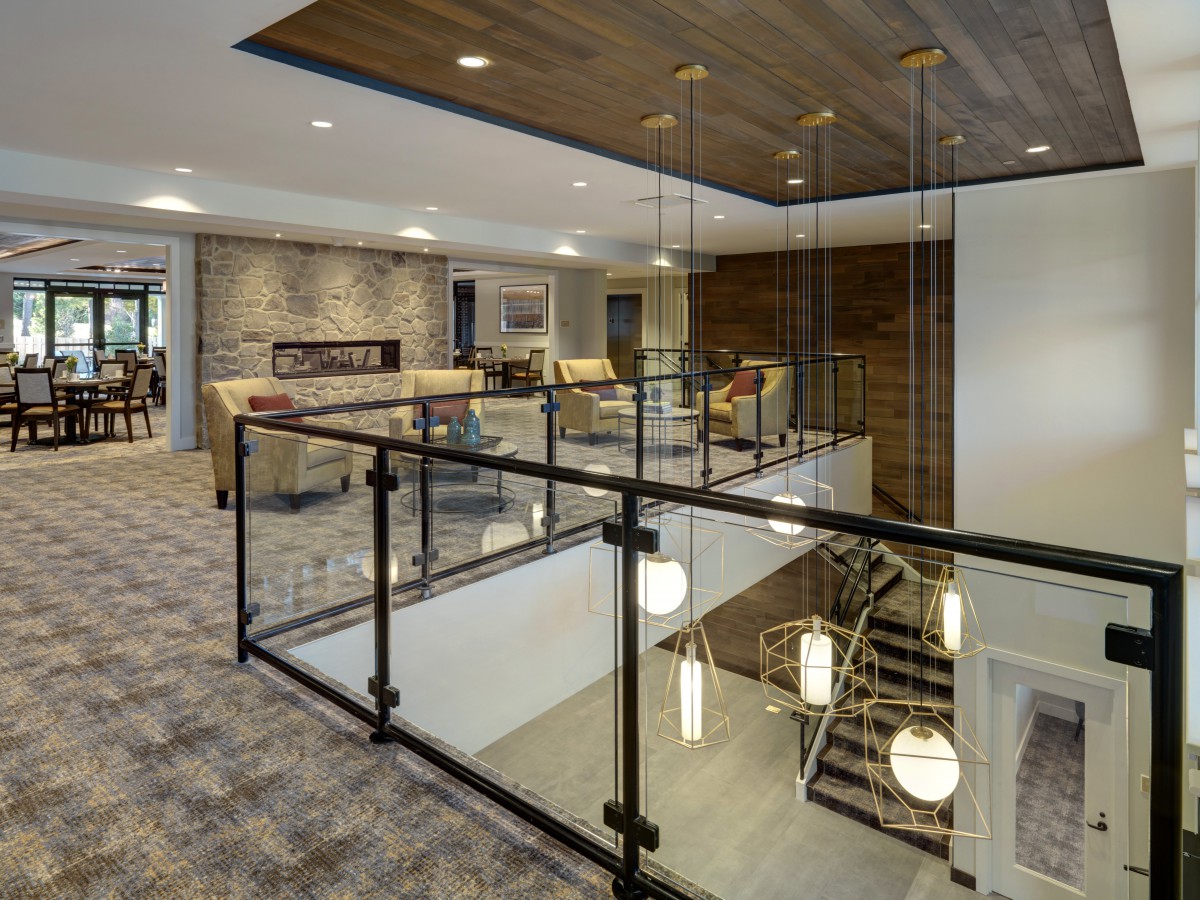 A modern lobby features a spacious seating area with stylish lighting, carpeted floors, and wood paneling.