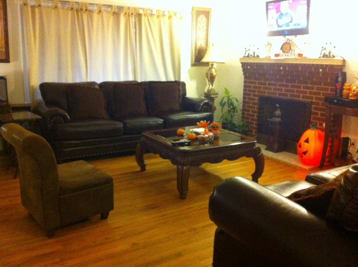 A cozy living room featuring a dark sofa set, wooden coffee table, and a brick fireplace with Halloween pumpkin decoration.