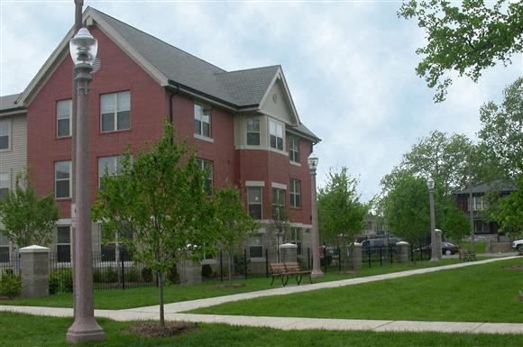 A brick residential building surrounded by a green lawn with trees and a sidewalk.