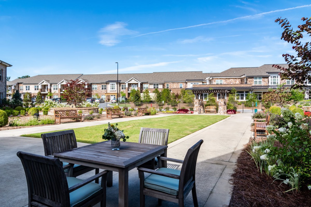 A tranquil patio setting in a residential neighborhood, featuring outdoor furniture and a well-maintained garden under a clear blue sky.