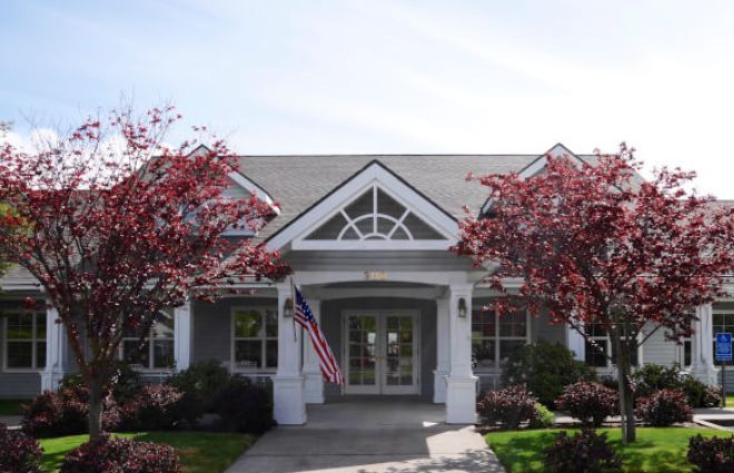 A charming house with a symmetrical front design, flanked by trees and displaying an American flag.