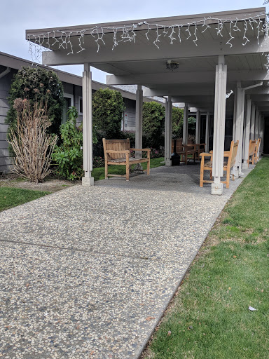 A serene outdoor patio area featuring wooden chairs and a gravel pathway, surrounded by greenery.