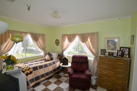 A cozy bedroom featuring a bed, recliner, and natural light from large windows.