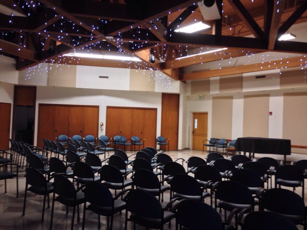 An empty conference room with rows of chairs arranged for an event, featuring decorative lights overhead.