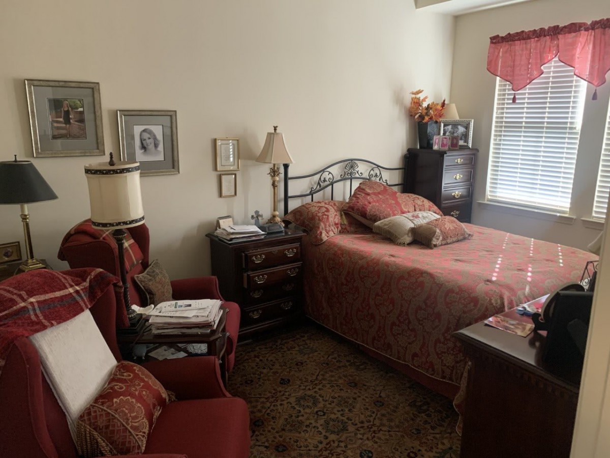 A cozy bedroom with a single bed, armchair, and decorative elements such as lamps and framed pictures.
