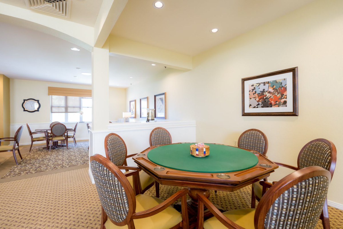 A spacious room featuring a poker table surrounded by chairs, with artwork on the walls and ceiling lights illuminating the space.
