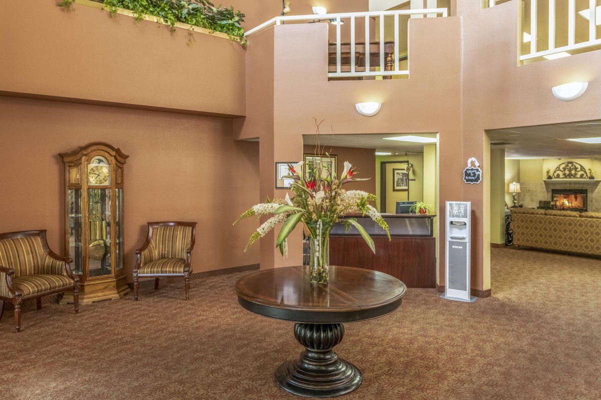 A hotel lobby with a central table adorned with flowers, a reception desk, and seating area.