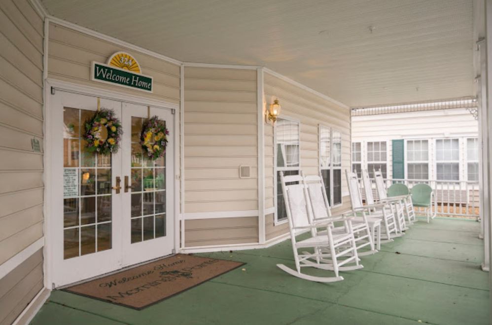A welcoming porch with rows of white rocking chairs and decorative wreaths on the entrance doors.