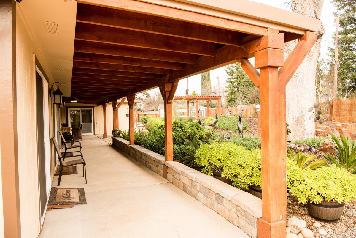A covered patio with wooden beams overlooks a well-maintained garden area.