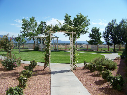 A serene outdoor garden featuring a beautifully crafted archway leading to a gazebo, surrounded by lush greenery under a clear blue sky.