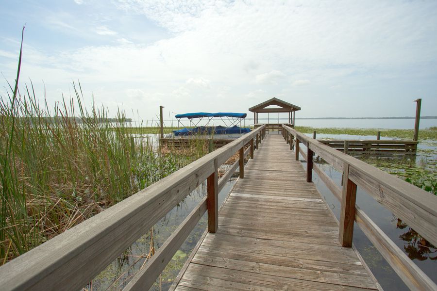 A wooden dock leading to a boat on a calm lake under a cloudy sky.