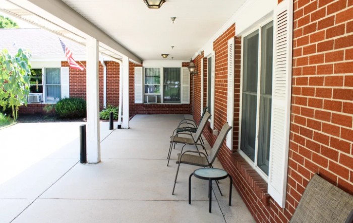 A covered porch with chairs against a brick wall and large windows.