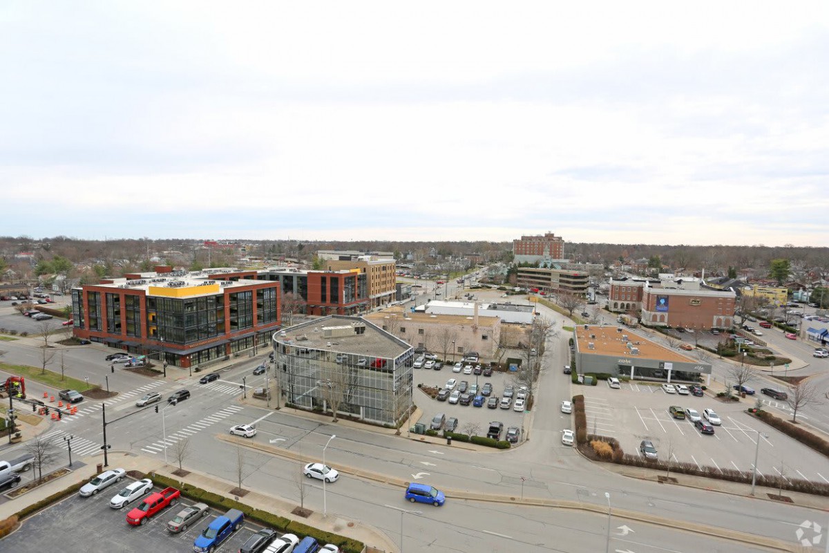 A view of an urban area with buildings, roads, and parking lots under a cloudy sky.
