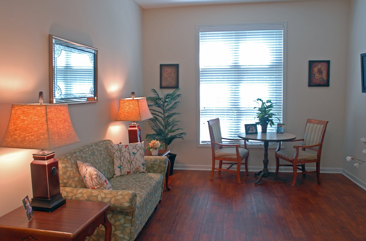 A cozy living room with a sofa, table, chairs, lamps, and decorative plants.