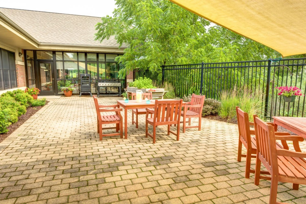 A sunny outdoor patio with wooden furniture surrounded by greenery.