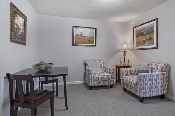 A cozy living room with patterned chairs, a small table, and decorative artwork on the walls.