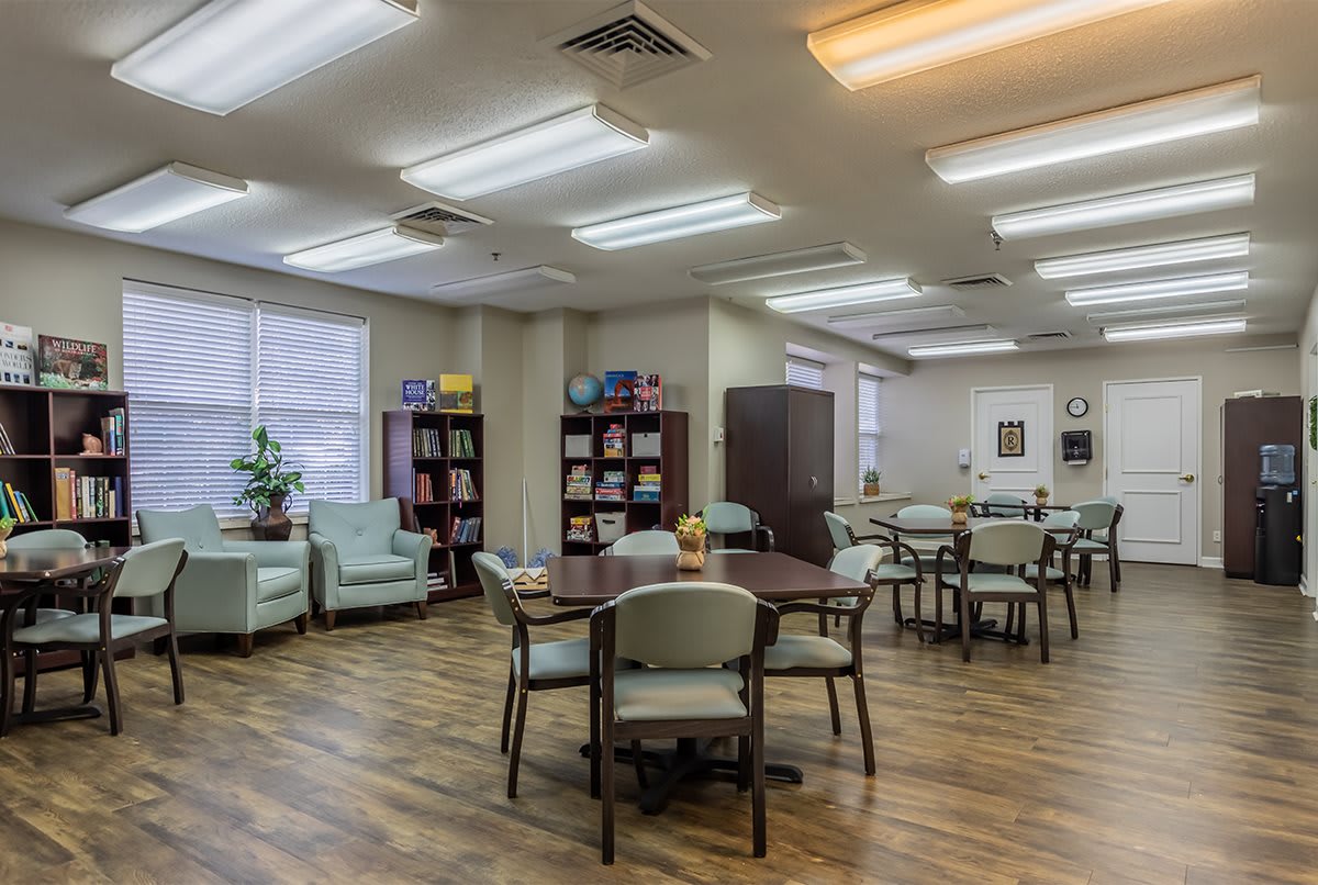 A cozy and well-lit lounge area with tables, chairs, bookshelves, and comfortable seating.