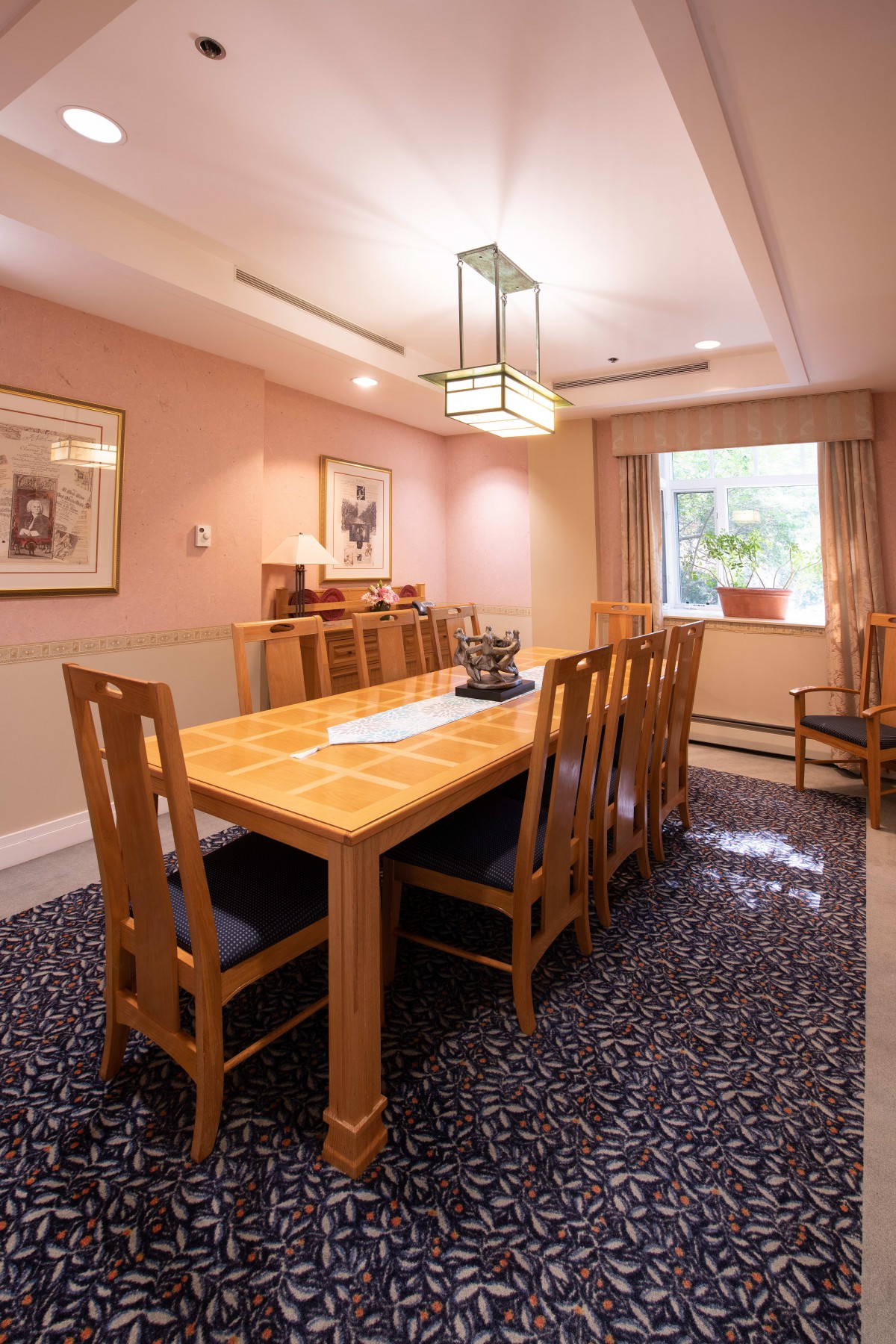 A cozy dining room featuring a wooden table and chairs, with artwork on the walls and natural light coming through the window.